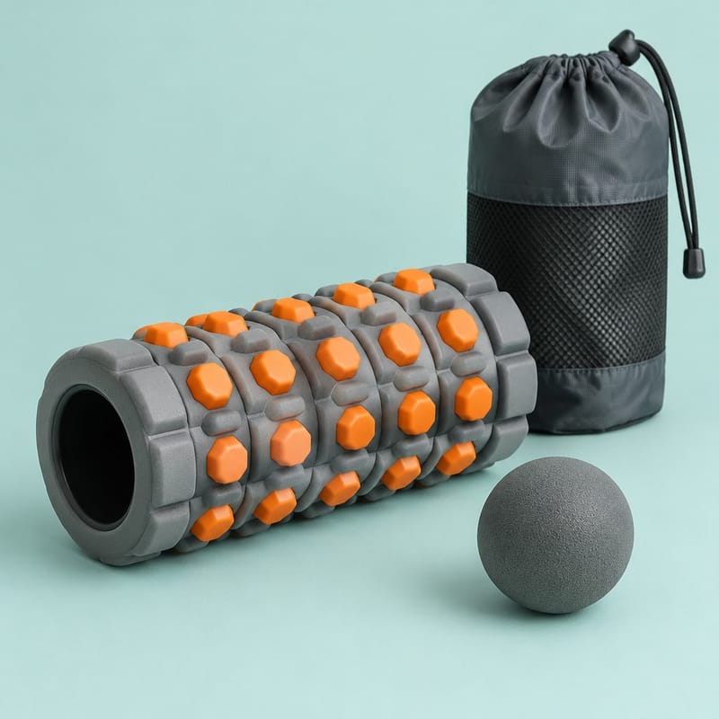 A grey collapsible foam roller with orange raised nodes beside a firm massage ball and a storage bag